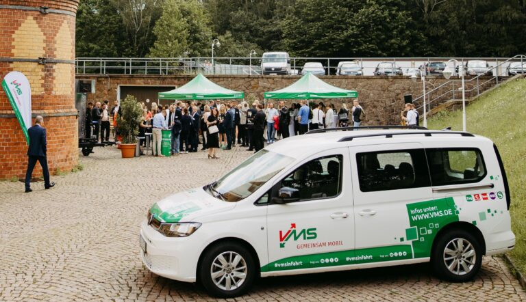 Auto mit VMS-Folierung steht auf einem Parkplatz vor einer Versammlung von Menschen